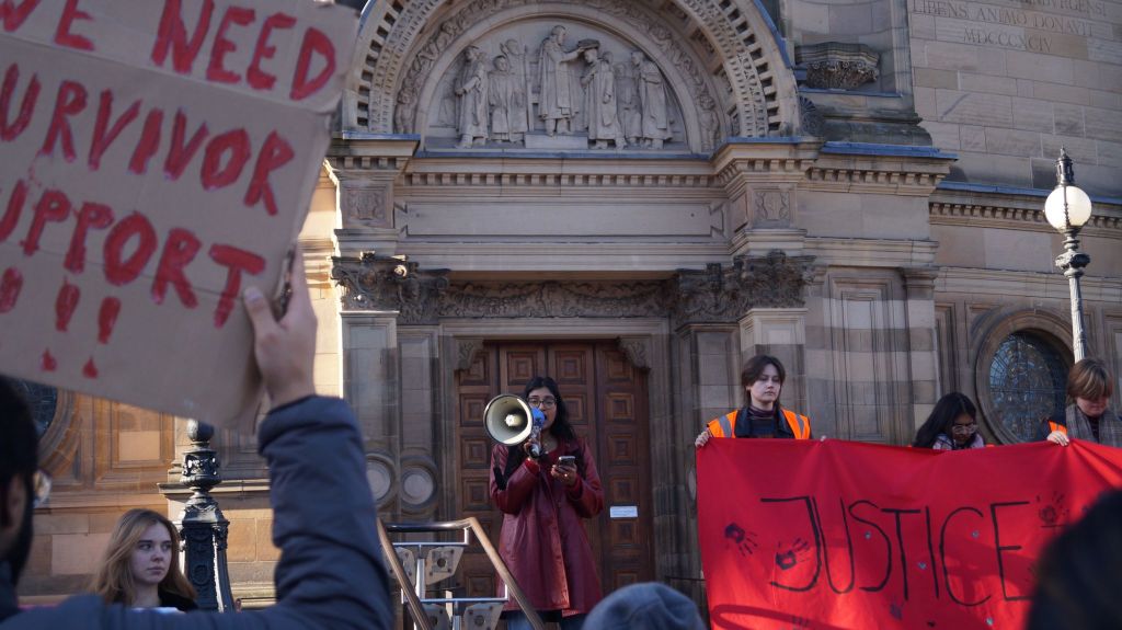 Student protestors standing outside McEwan Hall in Bristo Square holding a red banner with the word ‘Justice’.